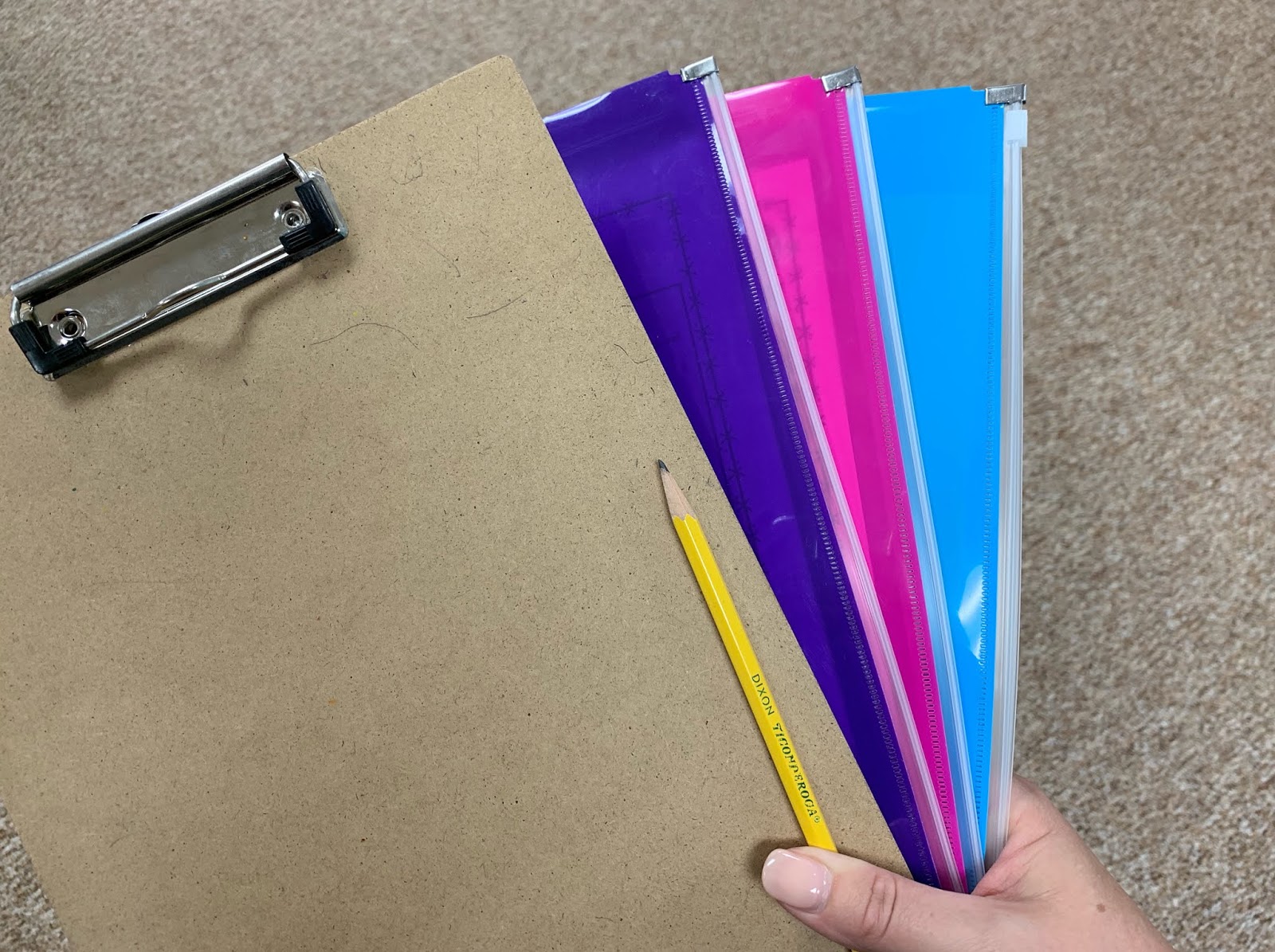 Teacher holding a clipboard, pencil, and three plastic zippered pouches
