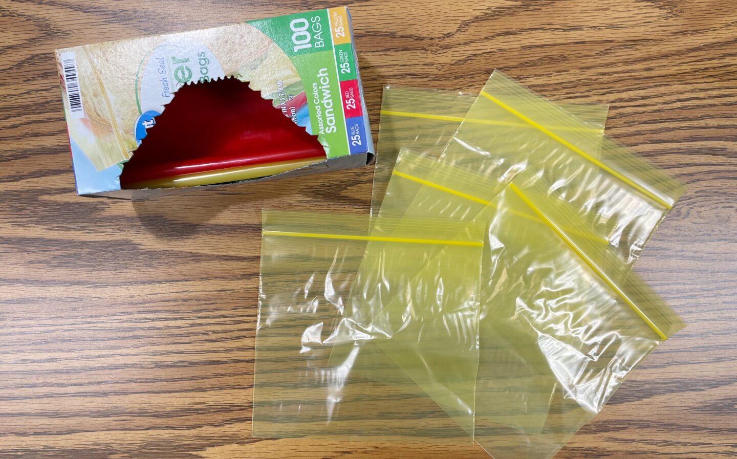 Image of Colored Sandwich Bags in Box with 5 Yellow Sandwich Bags laid on a Desk